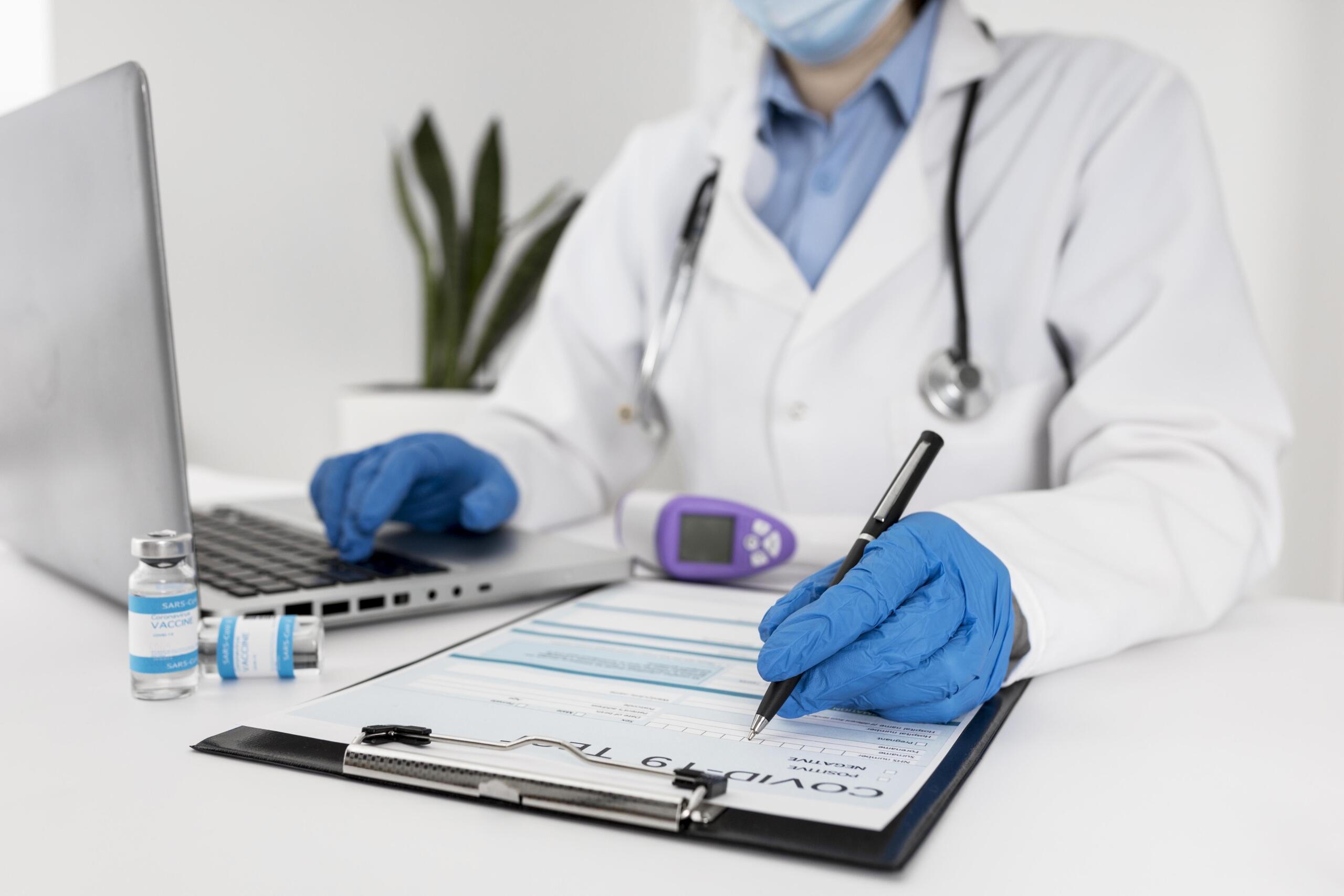 Toma detalle de manos de un médico de laboratorio revisando unos análisis con una laptop y lapicero