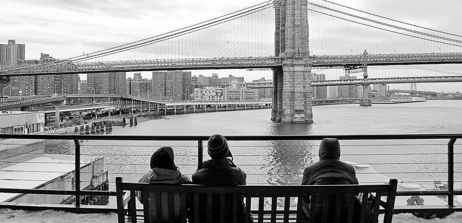 Foto en blanco y negro, tres personas sentadas en una banca mirando hacia el puente de San Francisco