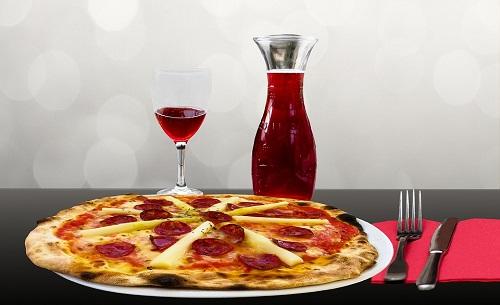 Fotografía imitando un bodegón, Copa y jarra de vidrio con jugo de uva y una pizza en frente.