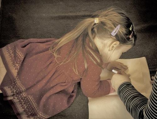 Niña de vestido rojo dibujando sobre un sofa.
