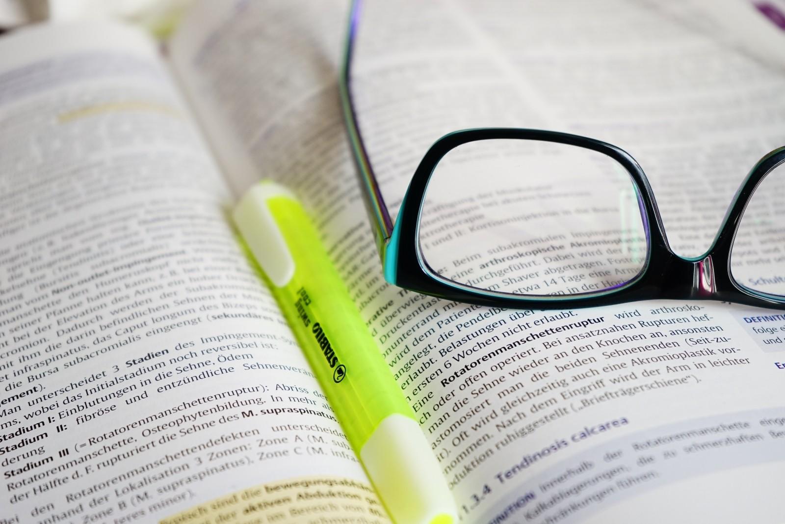 Lentes sobre un diccionario y un resaltador verde.