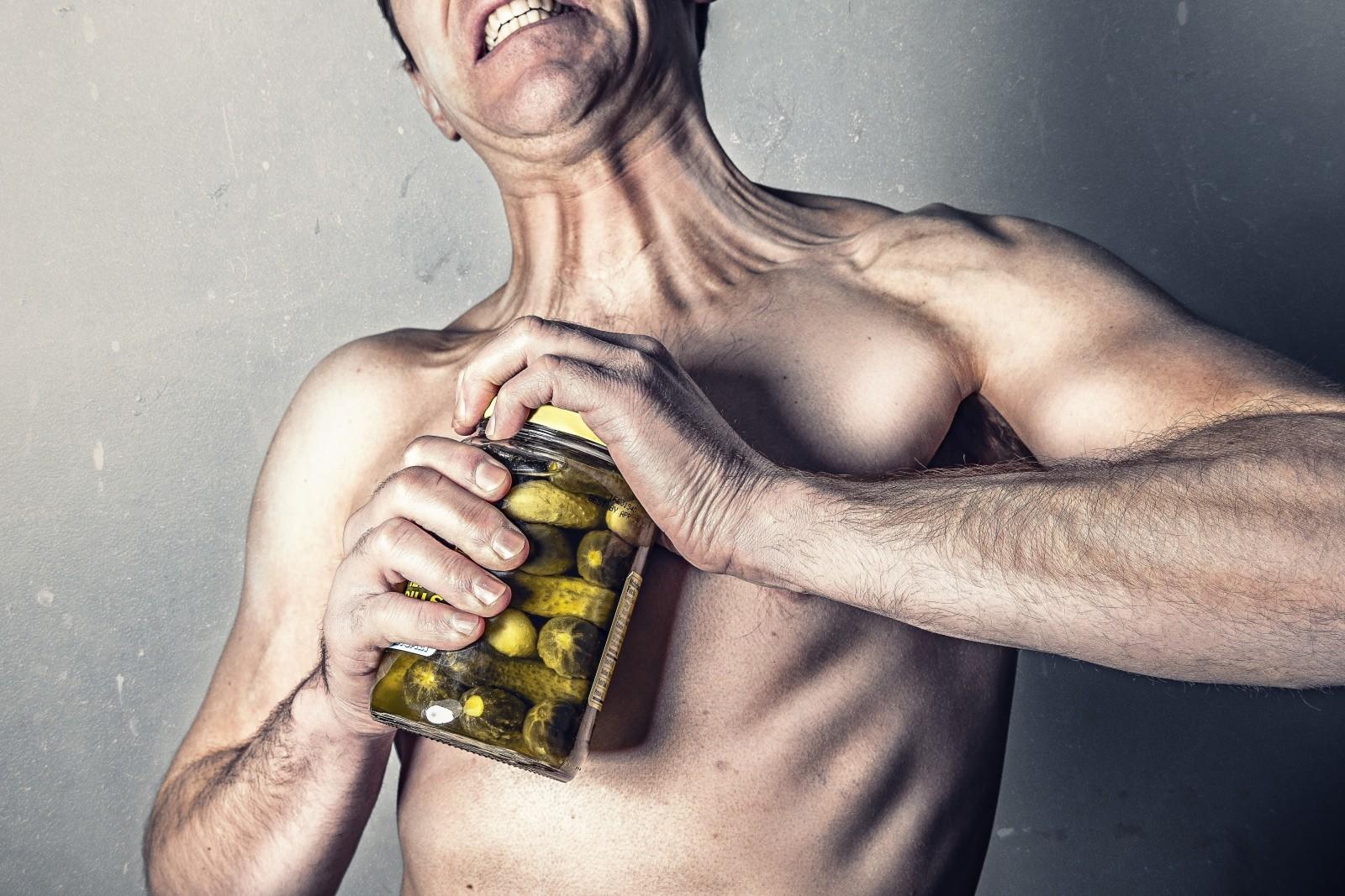 Hombre intentando abrir un tarro de aceitunas, mientras que a su vez ejercita sus brazos.