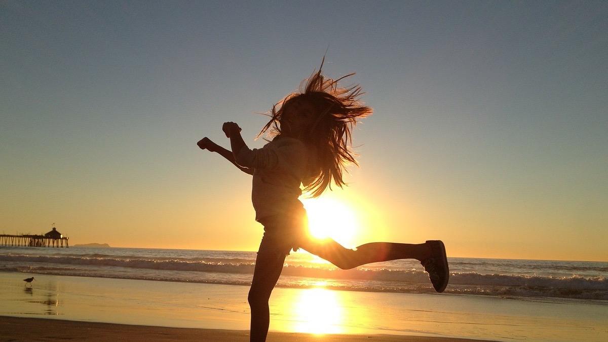 Silueta de una mujer bailando en la playa a contra luz del sol.