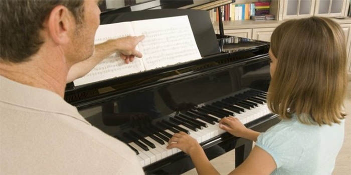 Profesor mostrándole ejercicios a niña para leer partitura de piano a primera vista