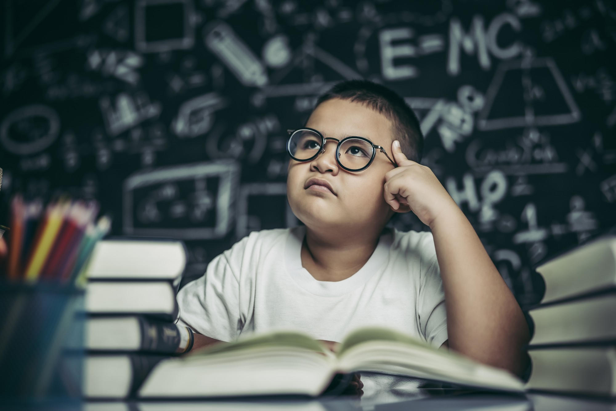 Niño frente a un tablero y junto a muchos libros pensando