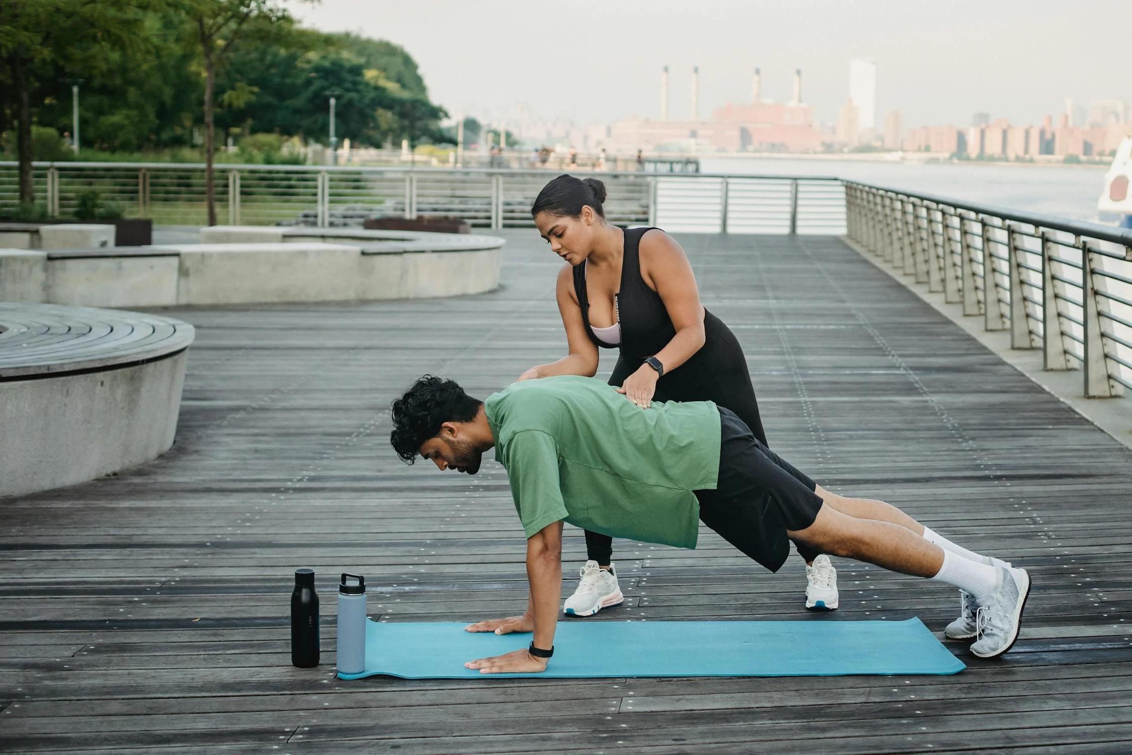 Entrenadora personal con un persona haciendo ejercicio sobre una colchoneta al aire libre