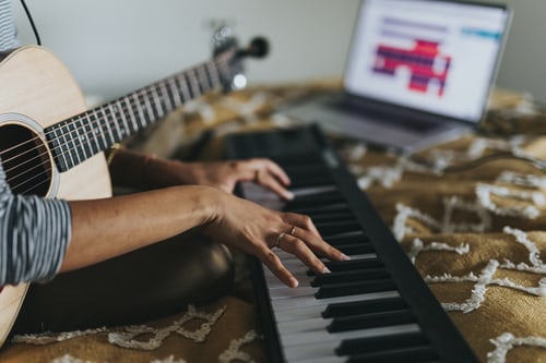 Persona sosteniendo una guitarra y tocando un teclado.