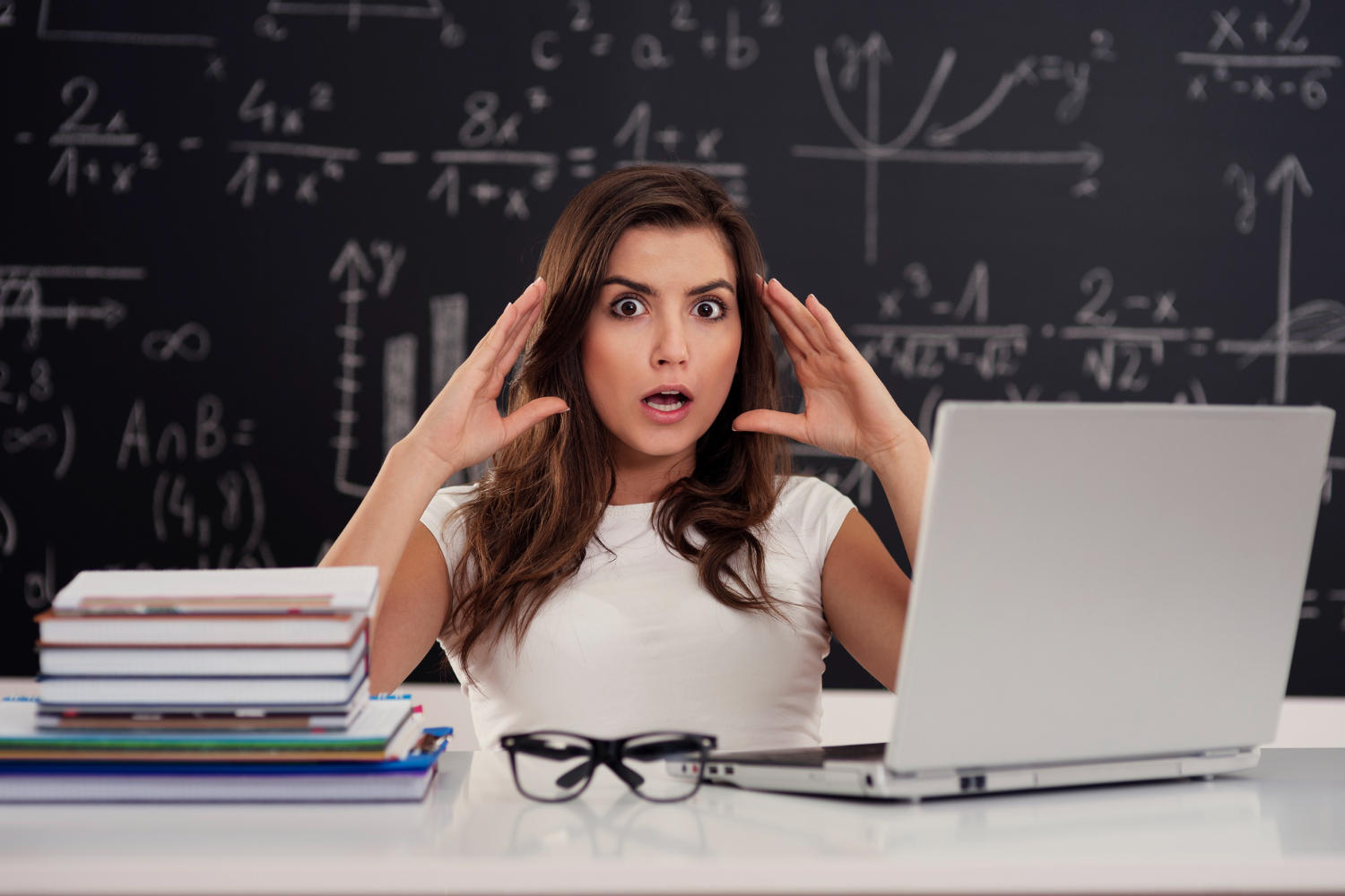 Mujer aterrada en aula de clase frente a una laptop tras el tablero