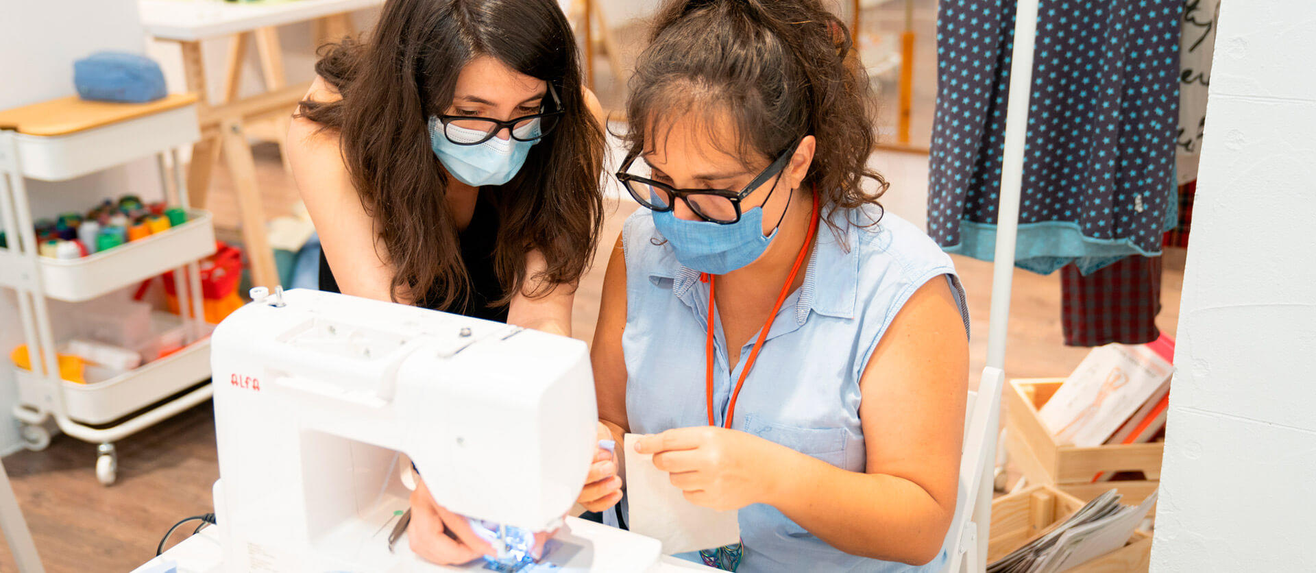 Dos chicas frente a una máquina de coser haciendo una prenda.