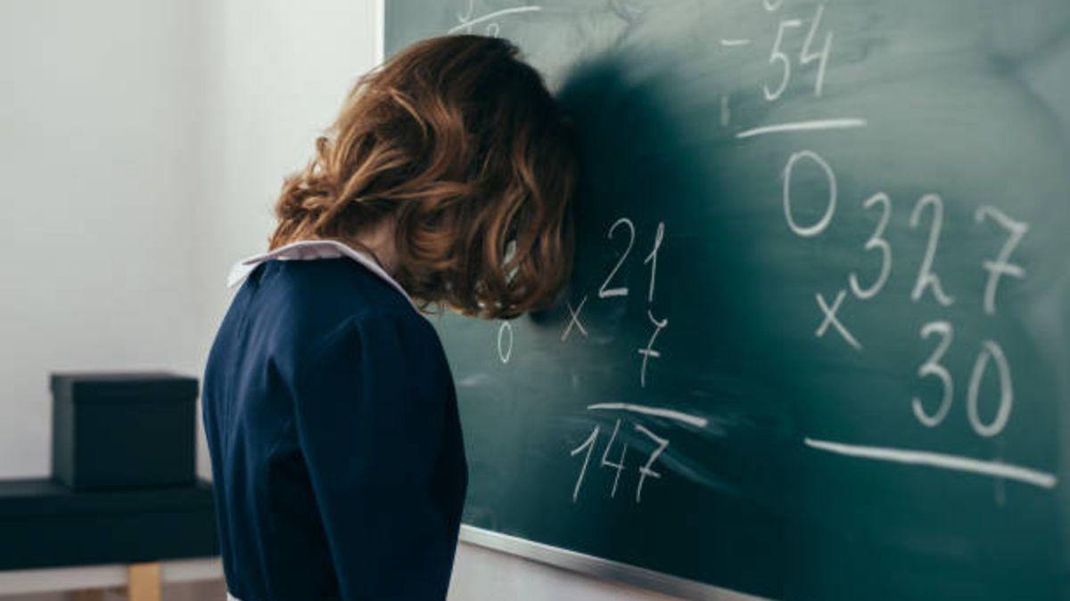 Chica tocando con su cabeza un tablero que contiene ejercicios matemáticos.
