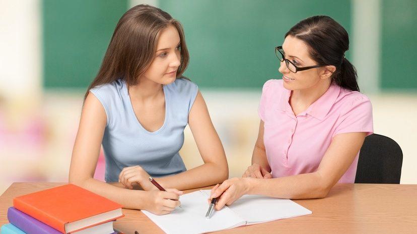 Profesora junto a una alumna observando unos apuntes.