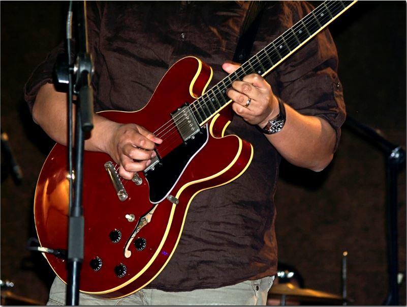 Hombre con camisa negra tocando la guitarra eléctrica roja