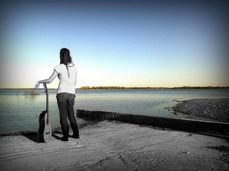 Mujer con guitarra mirando al horizonte de un gran lago