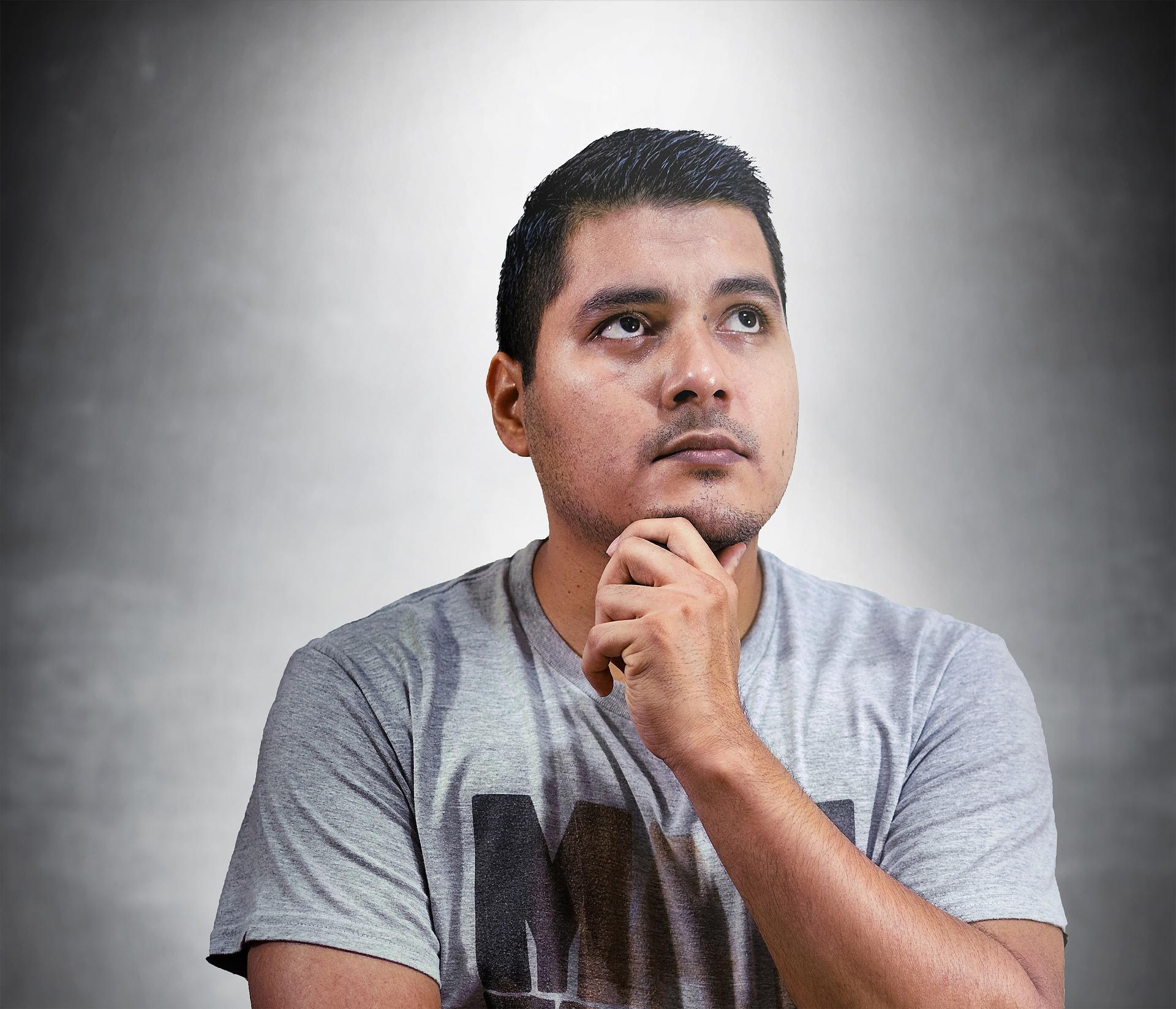 Hombre con su mano en el mentón, mirando hacia arriba, con una expresión pensante.