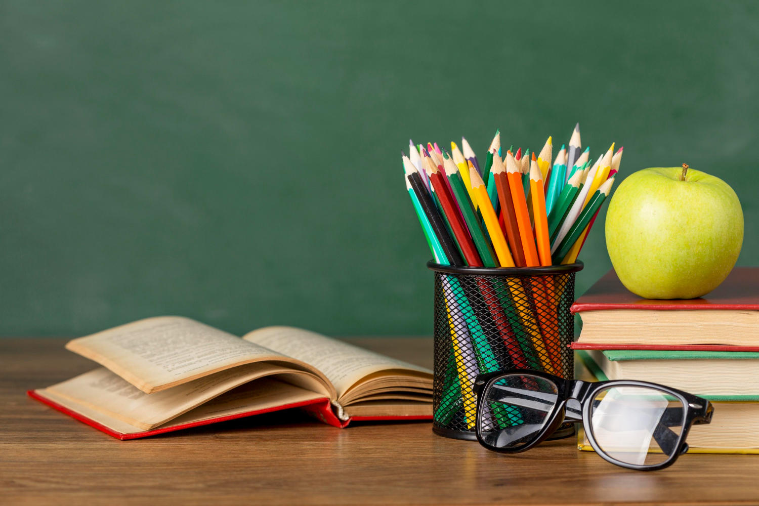 Escritorio de aula de clases con colores, libro abierto, manzana y gafas
