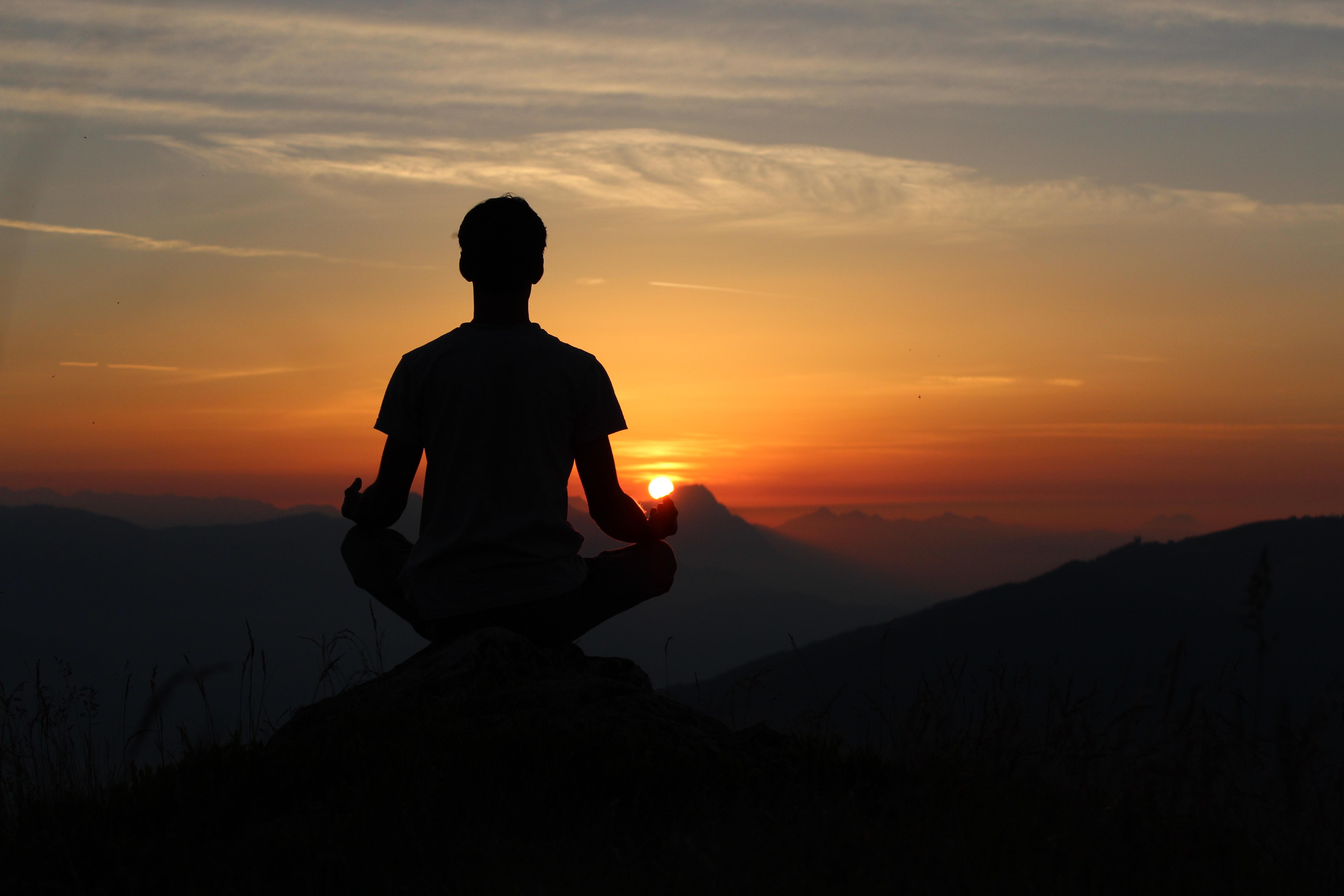 Silueta de un hombre meditando al atardecer.
