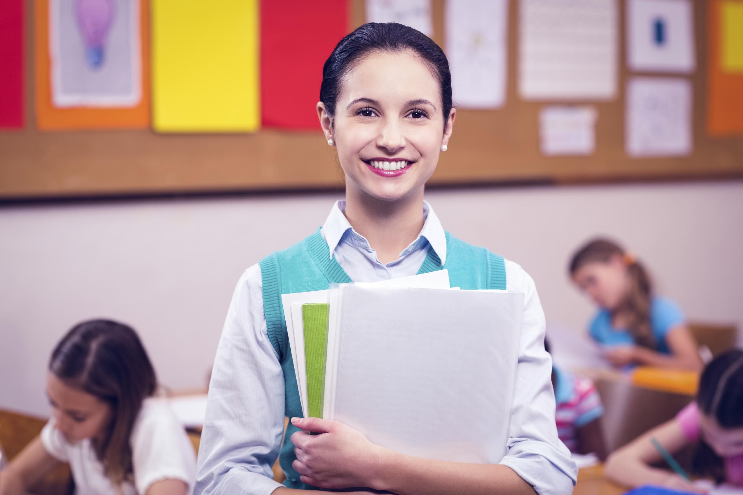Profesora sonriendo mientras sostiene en unos libros en sus manos.