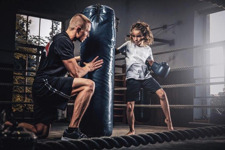 Entrenador sosteniendo el saco de boxeo mientras un joven deportista golpea el saco.