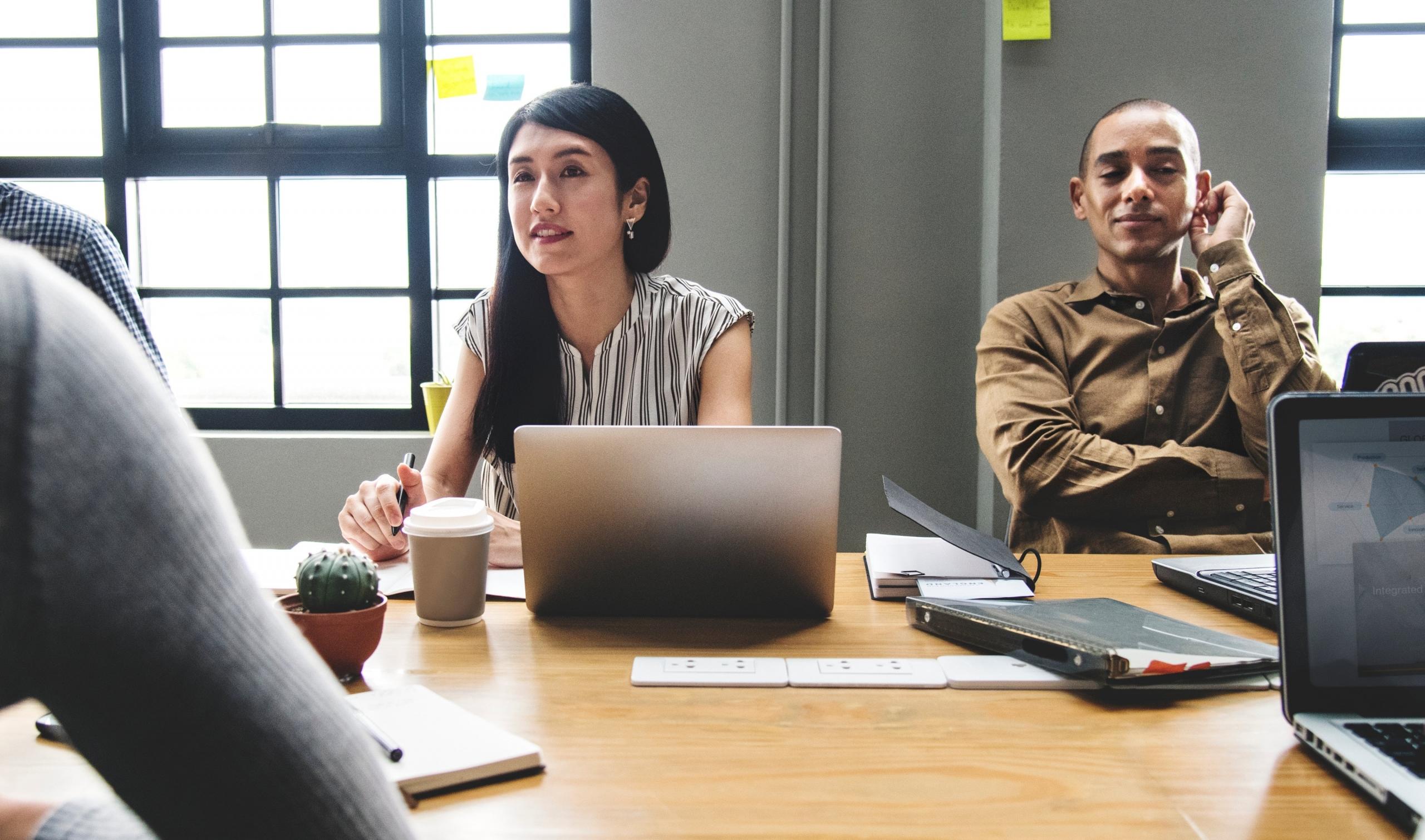 Chica asiatica y chico latino, sentados en una mesa trabajando juntos.