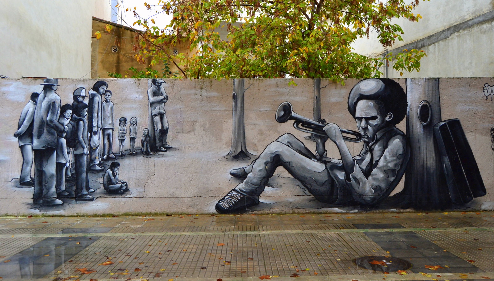 Pintura urbana sobre muro de la calle que muestra un hombre bajo un árbol tocando un clarinete