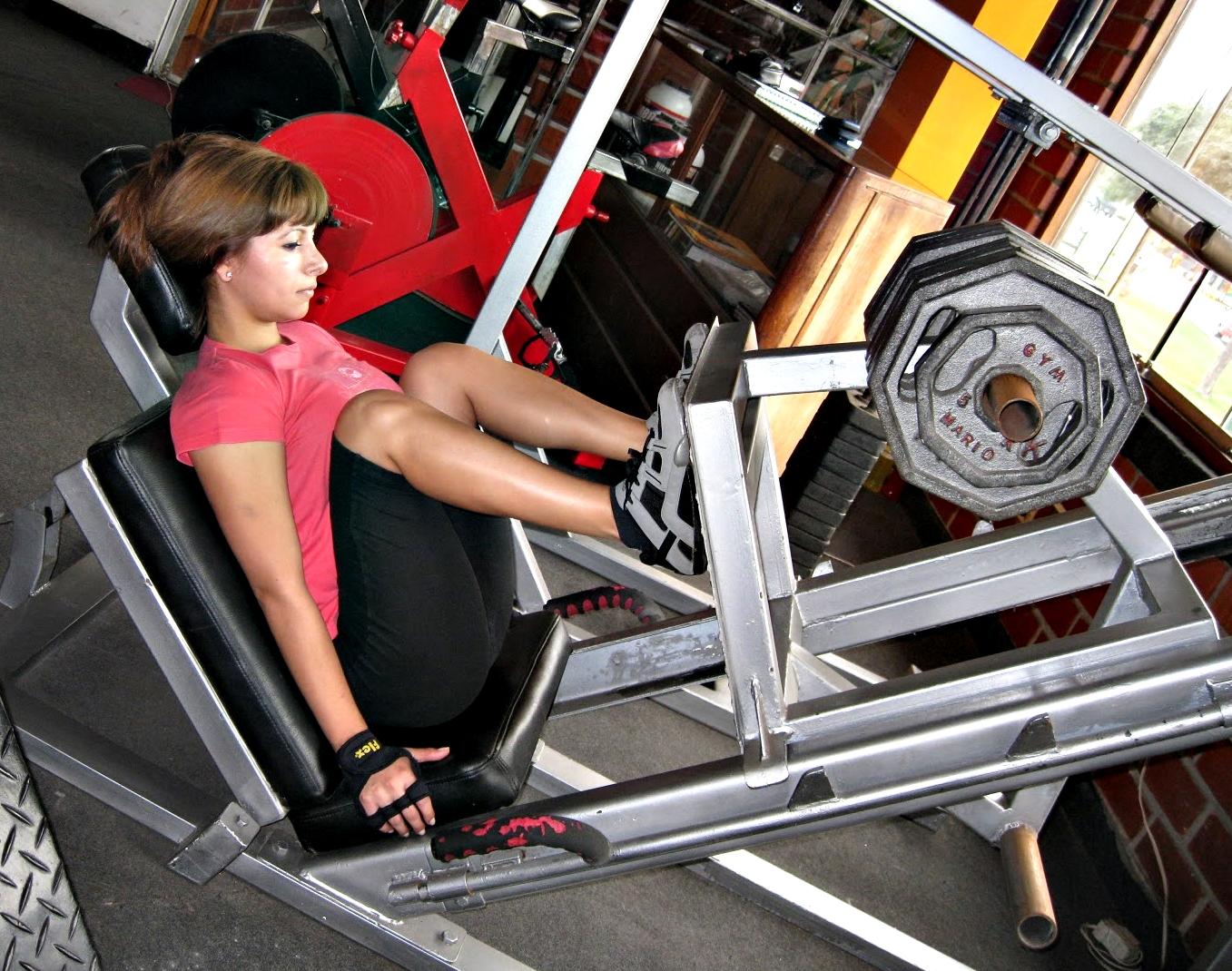 Chica haciendo entrenando en una máquina de prensa.