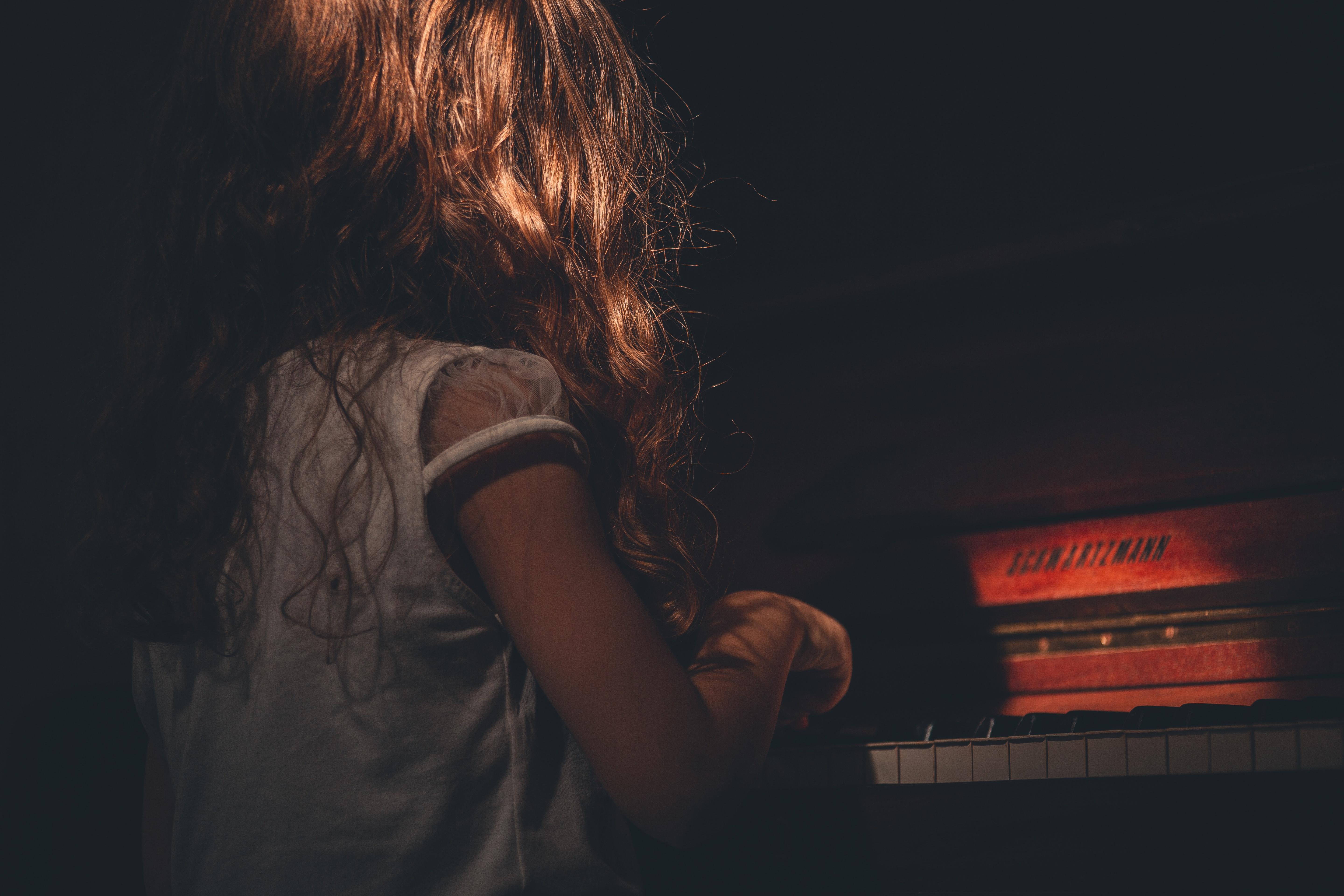 Niña de espaldas tocando el piano en la un ambiente con poca luz.