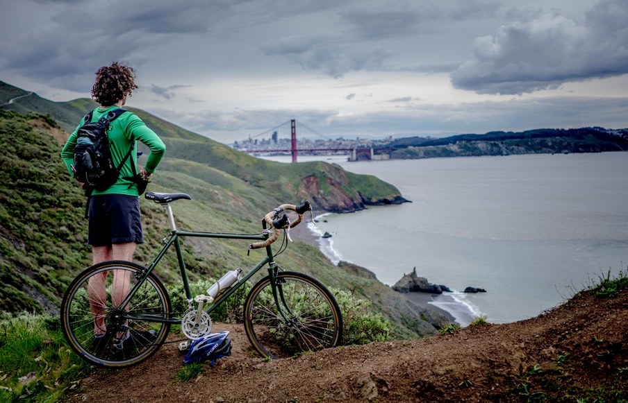 Hombre en su bicicleta, mirando hacia un puente colgante