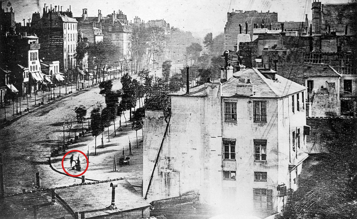 Edificio a blanco y negro visto desde lejos, con una persona parada a la derecha.