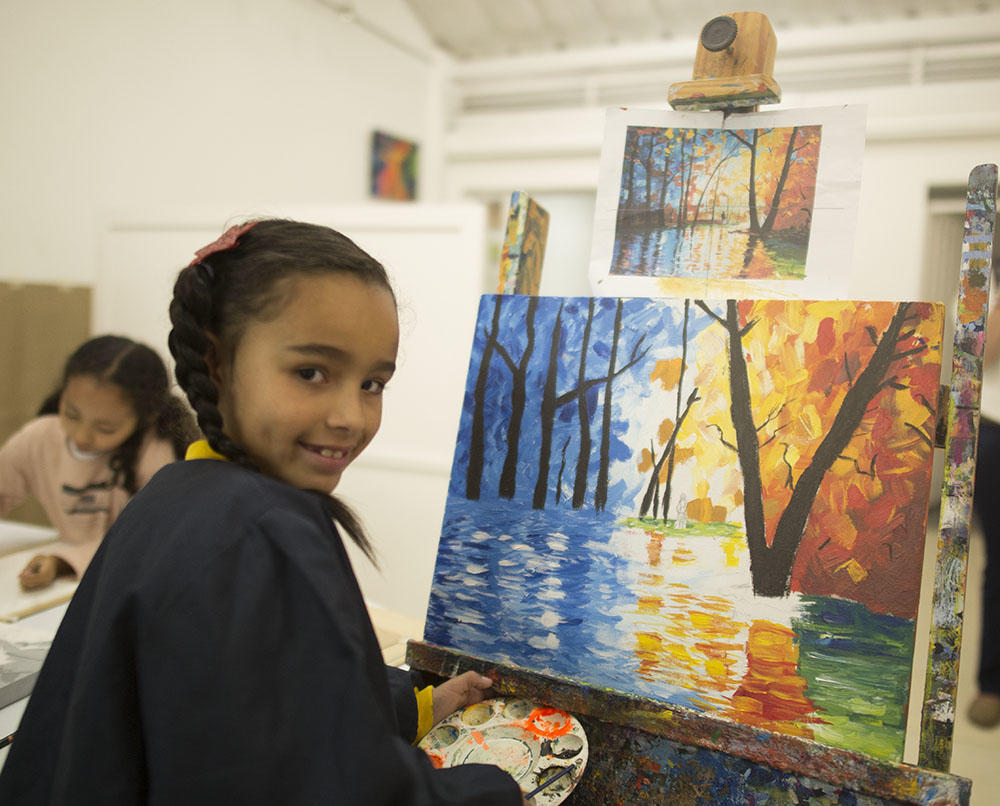 Niña sonriendo terminando un dibujo de un paisaje.