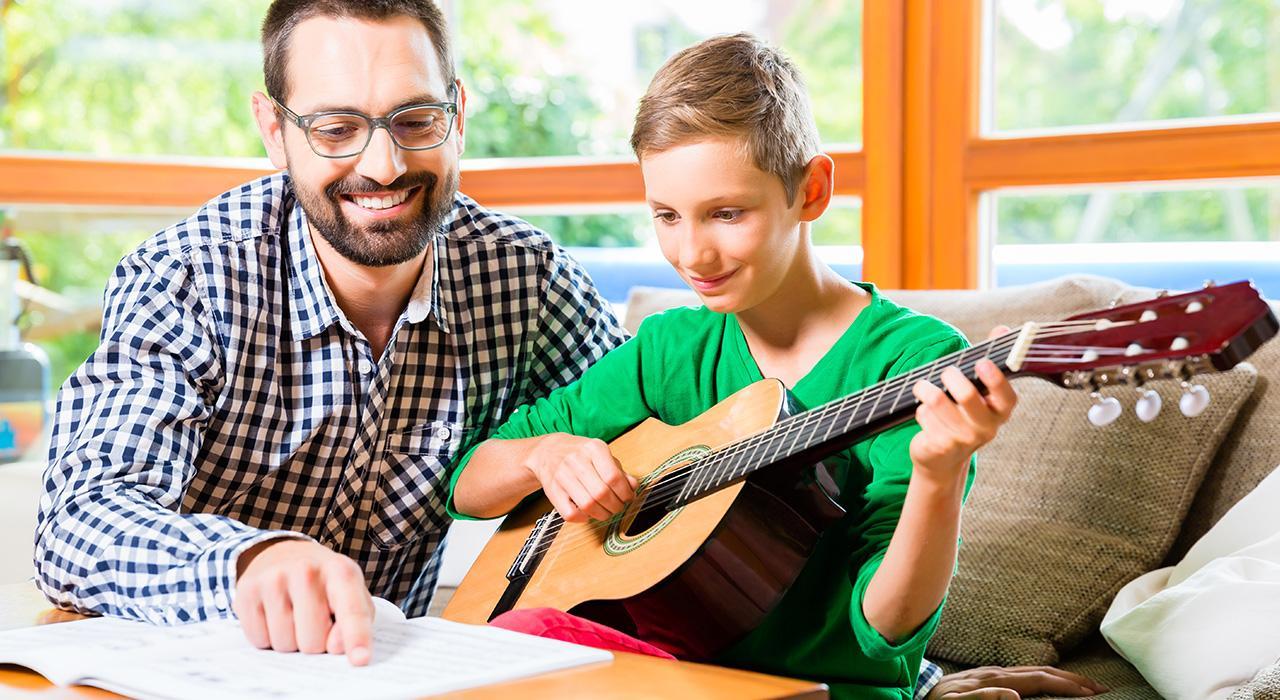 Chico aprendiendo a tocar guitarra en compañía de un profesor.