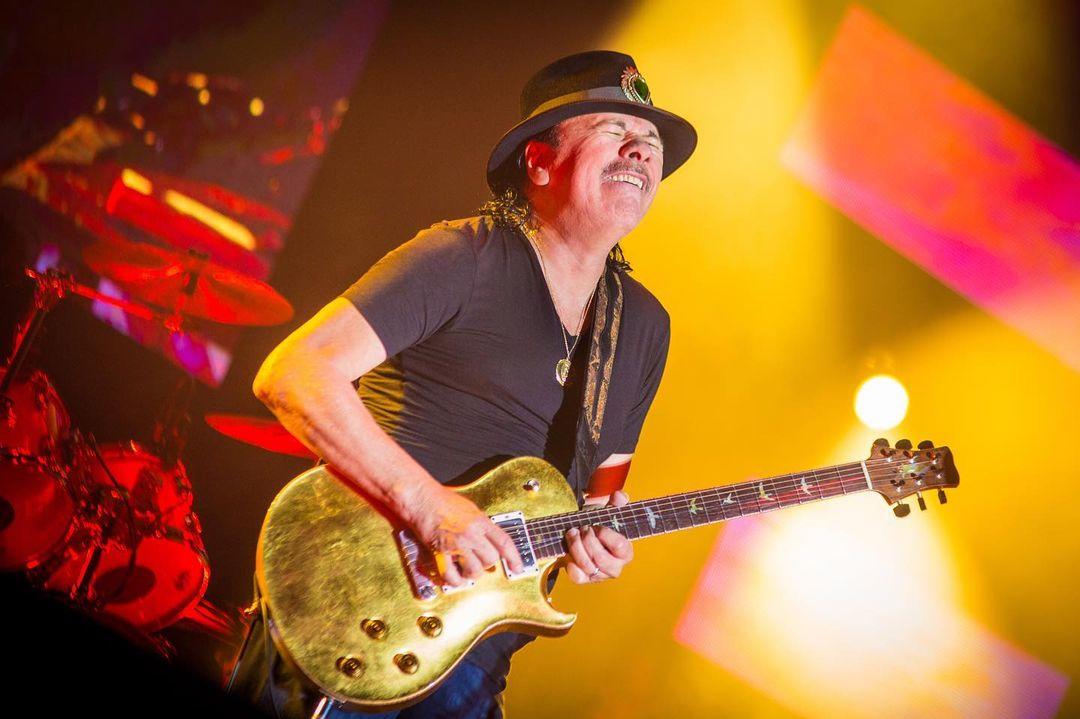 Santana tocando una guitarra dorada en un concierto.