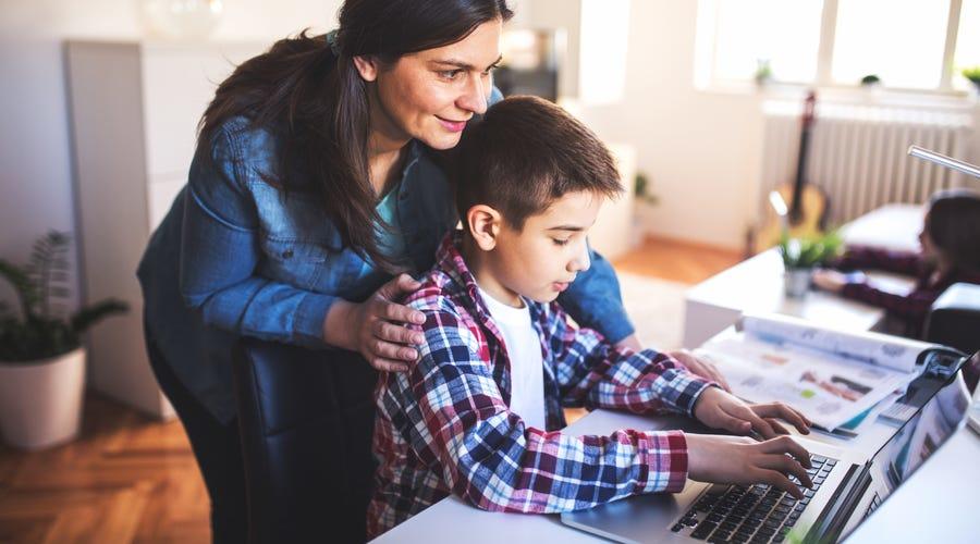 Madre guiando a su hijo frente a la laptop en una clase online