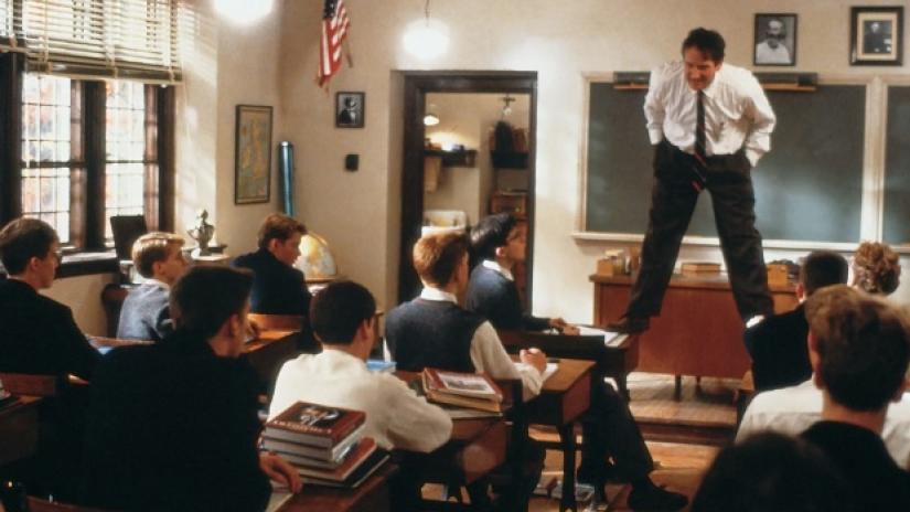 Profesor parado sobre los pupitres explicando a los chicos en la clase