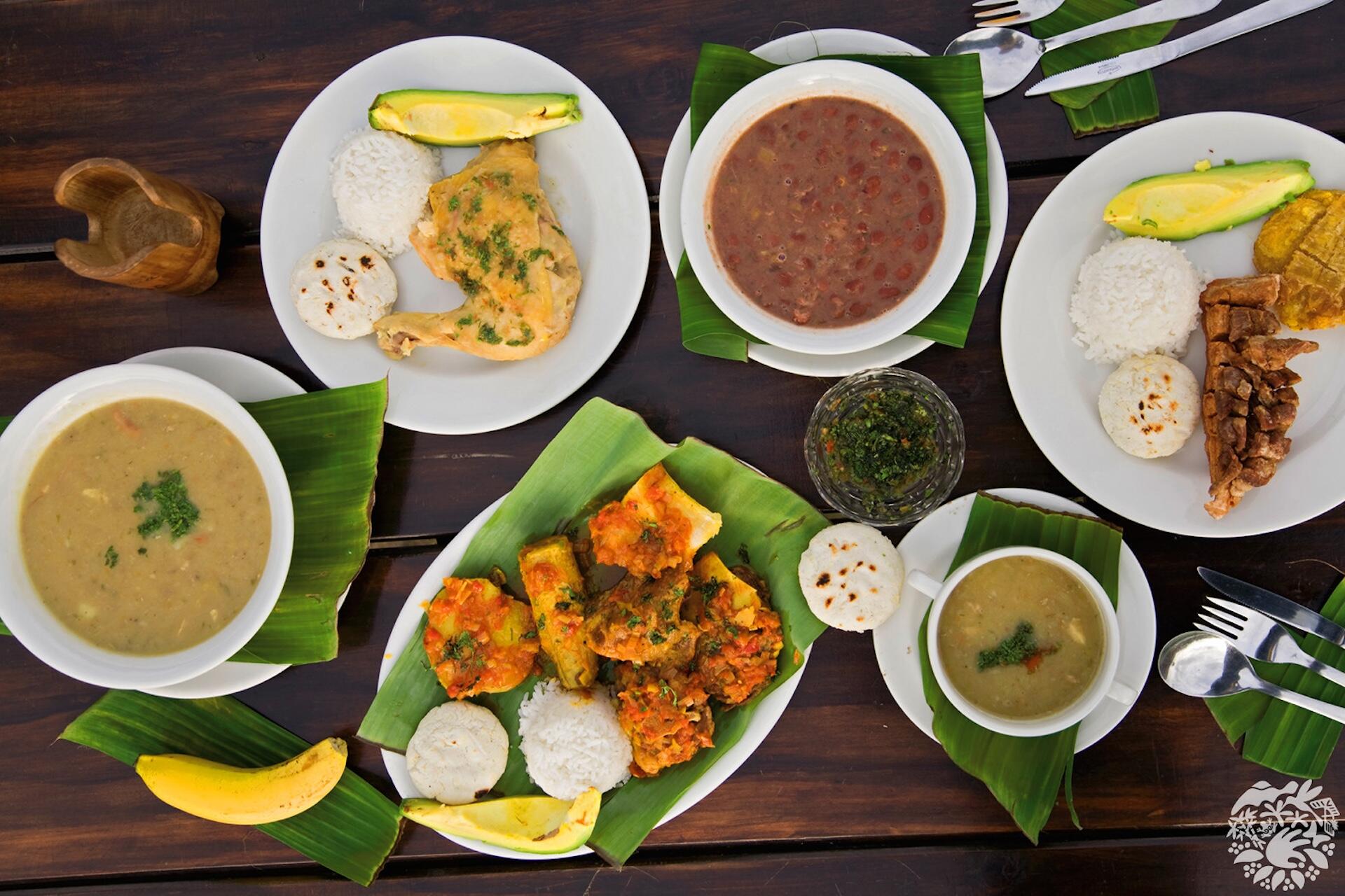 Imagen de una mesa con comidas típicas colombianas como frijoles, chicharrón, sancocho