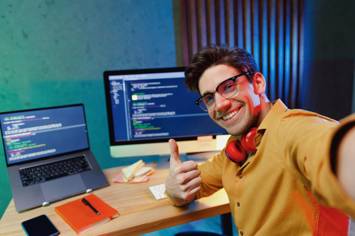 Programador sonriendo junto a una computadora que muestra un código binario.