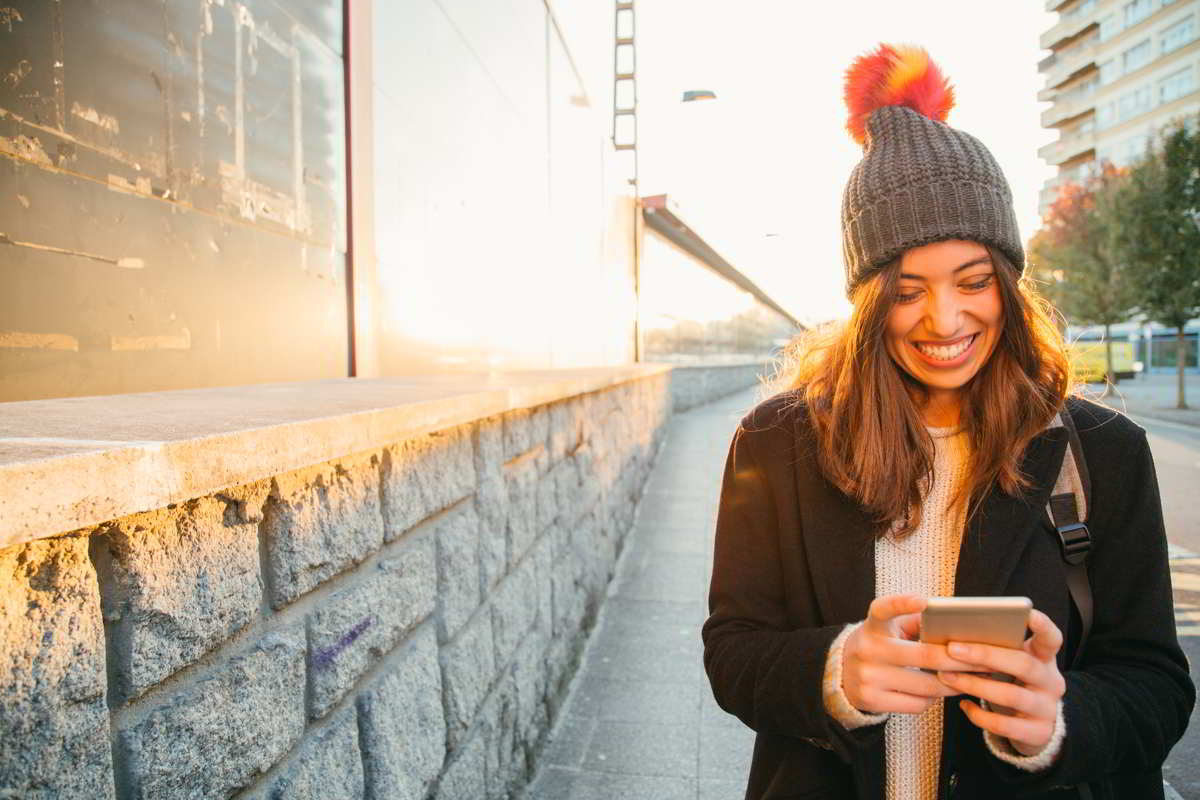 Chica caminando y sonriendo mitras usa su teléfono movil.