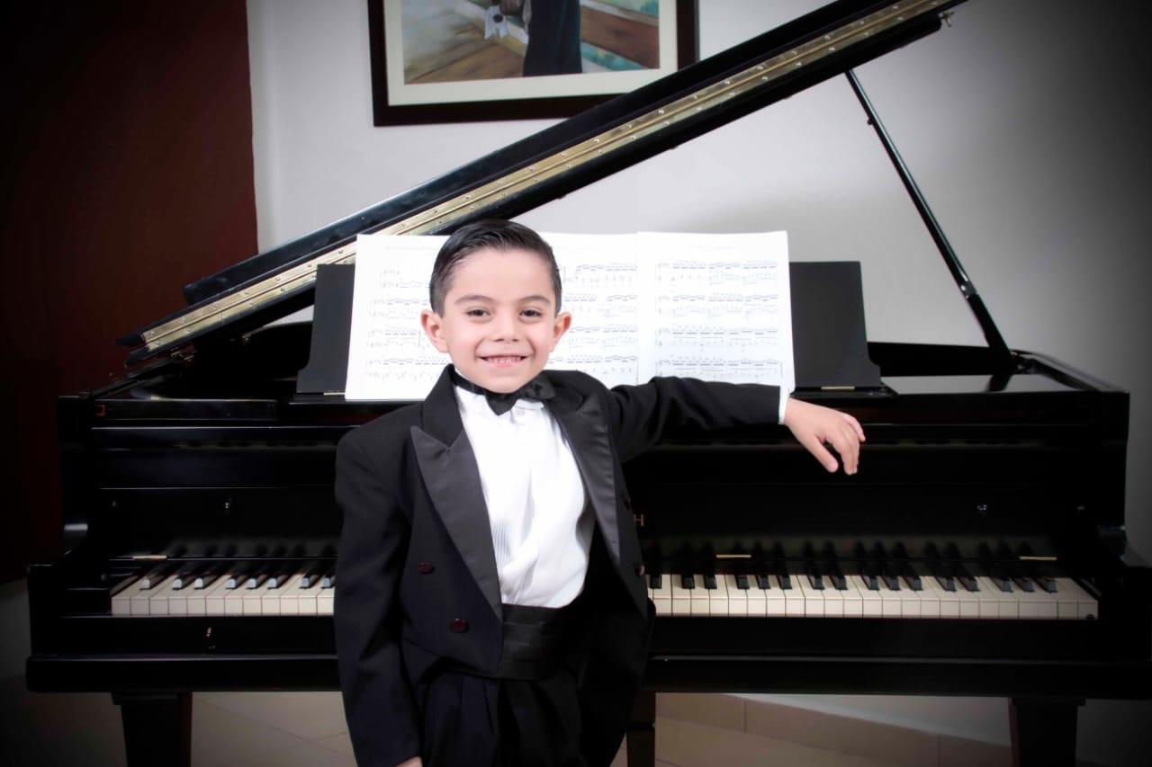 Niño vestido con smoking negro con el brazo sobre un piano