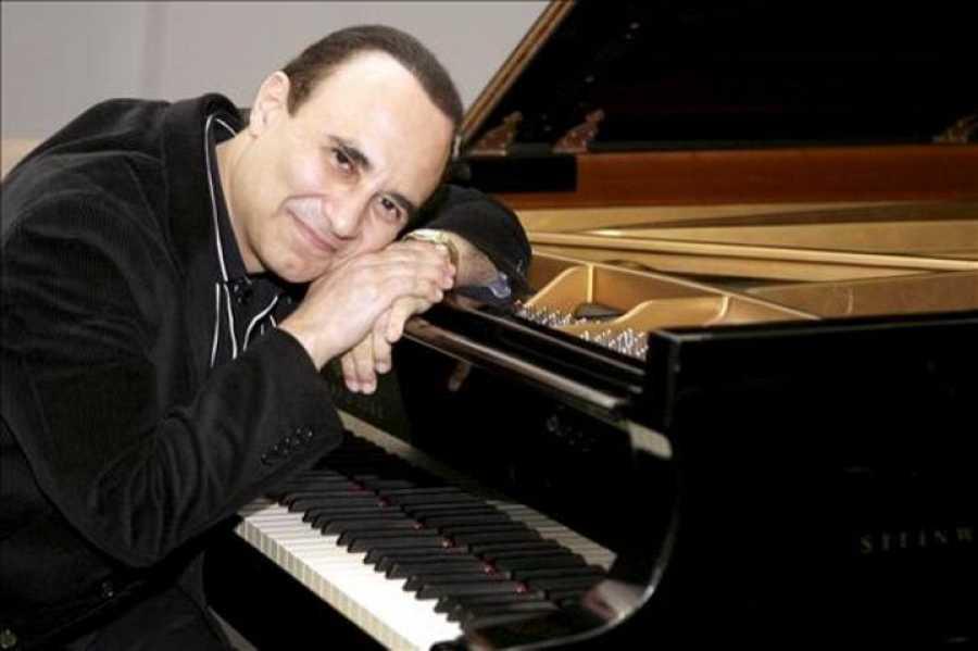 Michael Camilo recostado sobre su gran piano, el cual esta abierto