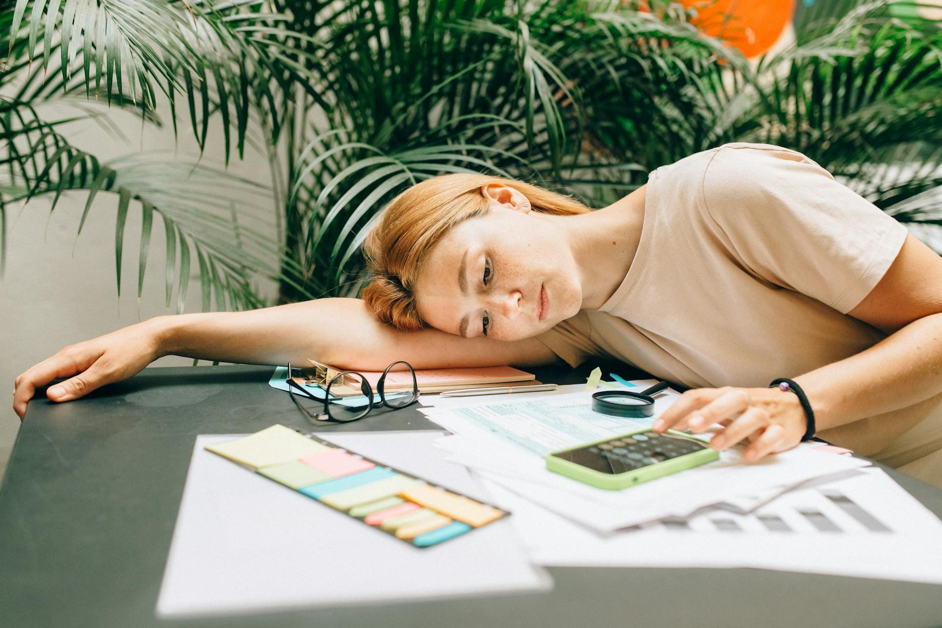 Mujer recostada en su escritorio realizando cuentas con una calculadora