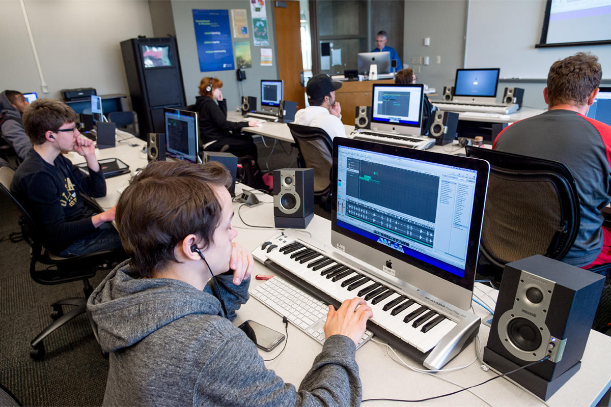 Varios estudiantes en salón con pianos