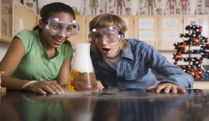 Personas que estudian química, observando con cara de asombro una reacción química.