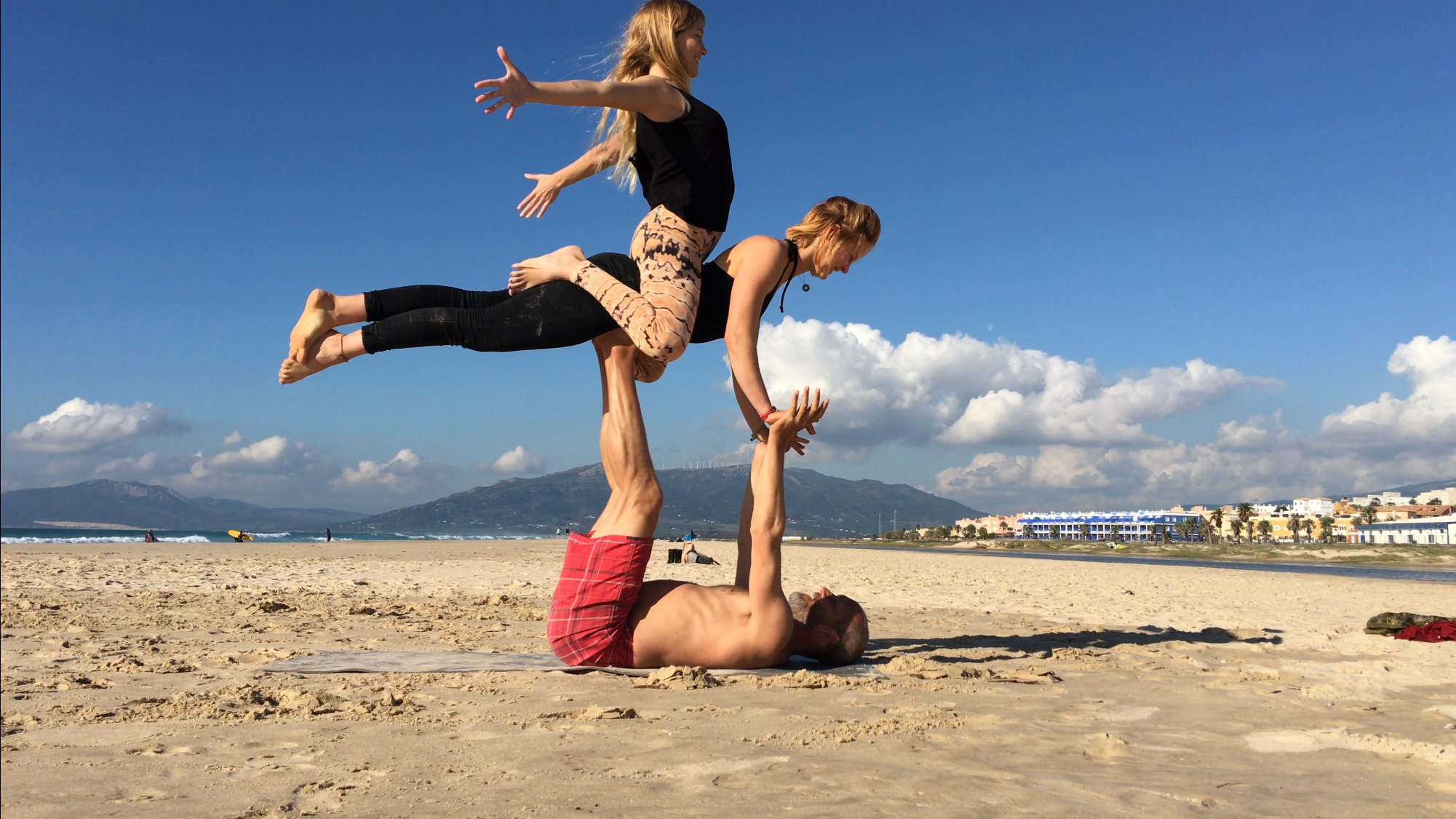 Tres personas haciendo movimientos de acroyoga en la paya