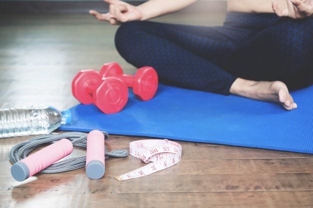 Mujer sobre el Mat de yoga, a su lado se ven la cuerda de saltar, las pesas, el metro y la hidratación