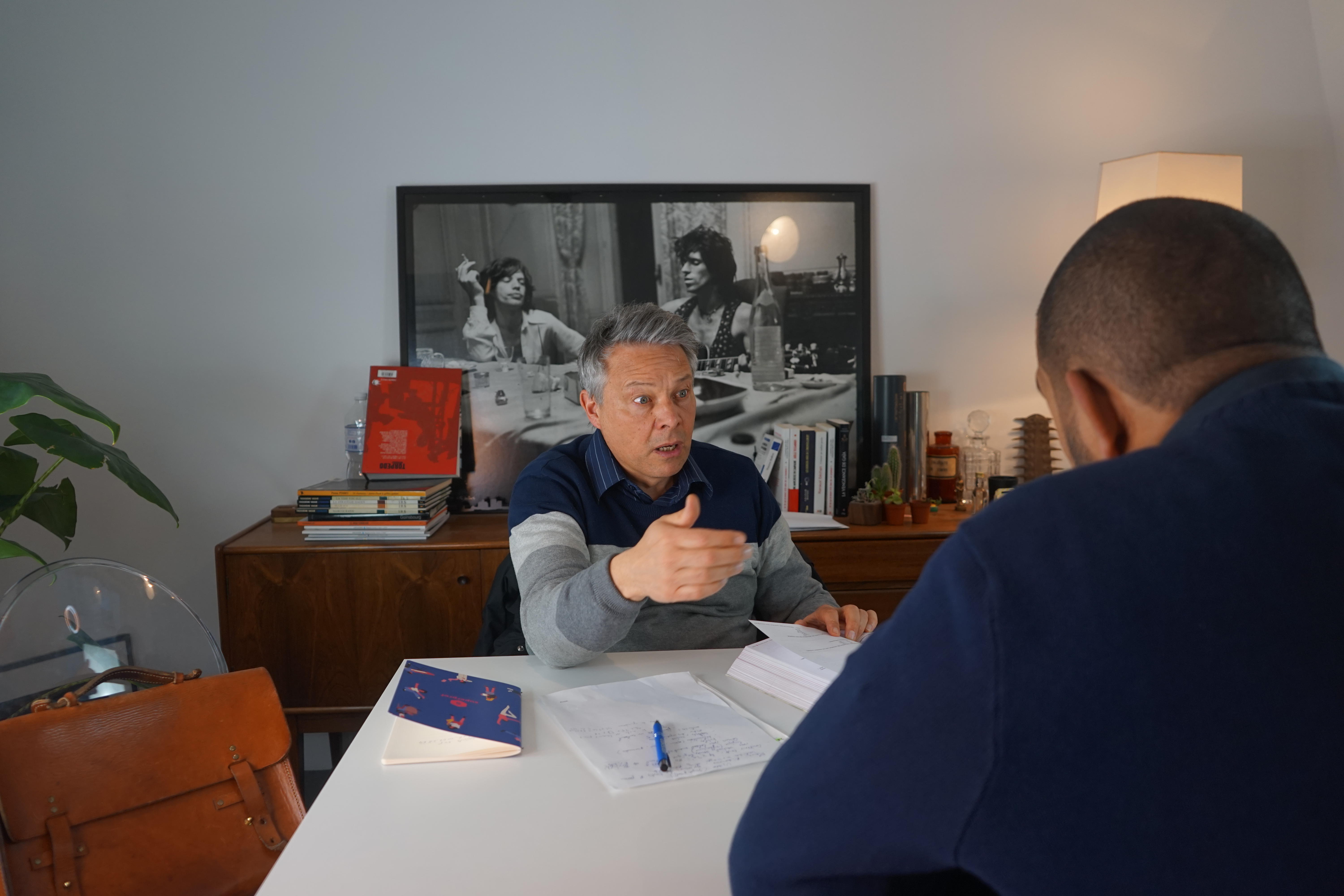 Profesor sentado detrás de un escritorio y frente a un alumno.
