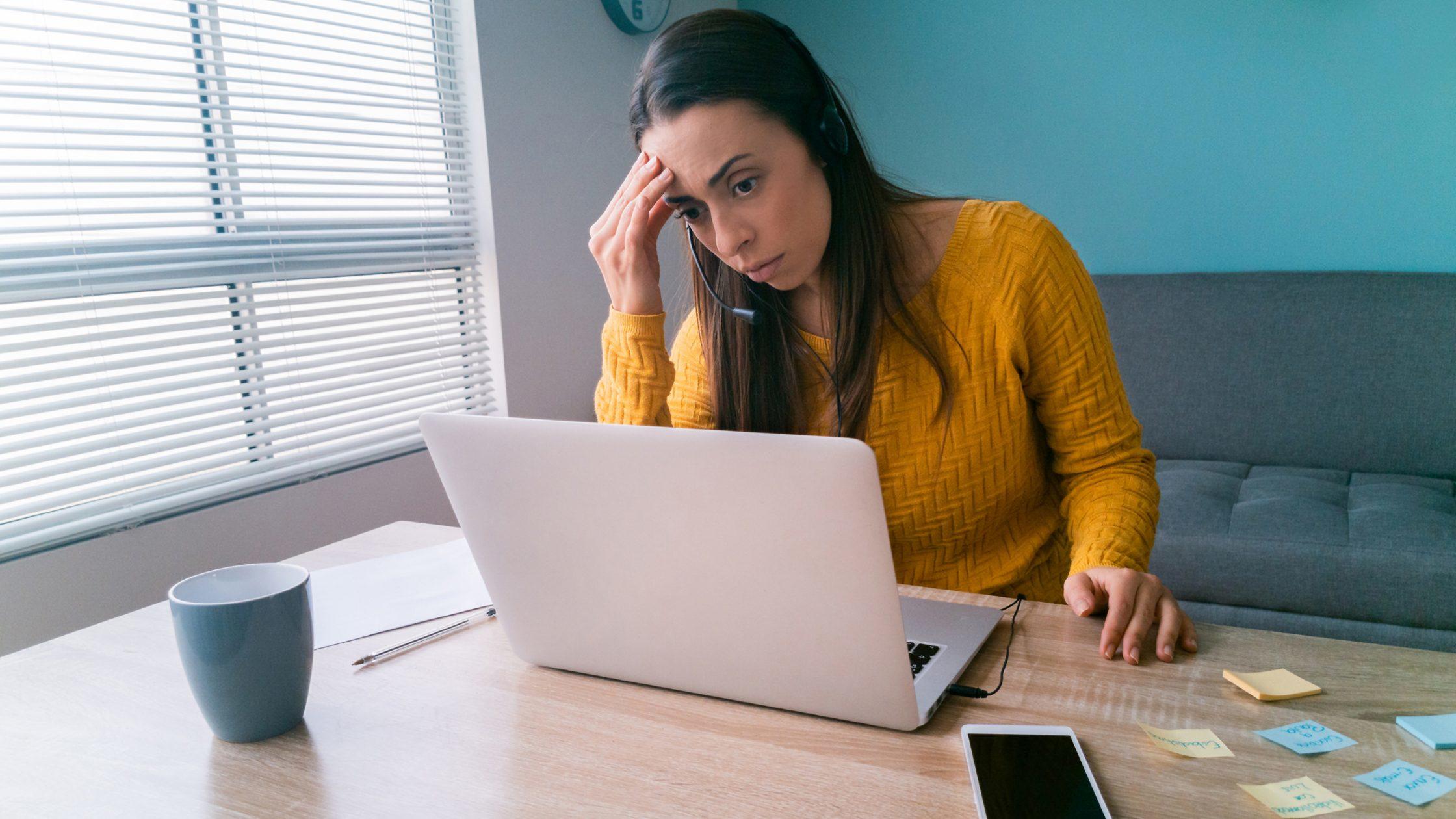 Chica frente a un portátil, con una mano en la frente y con expresion de preocupacion.