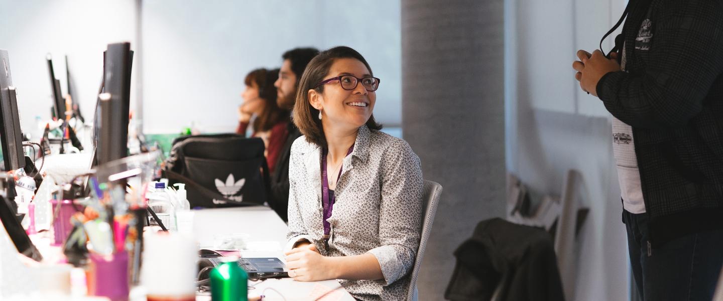 Mujer con una gran sonrisa en una oficina frente a su computadora.