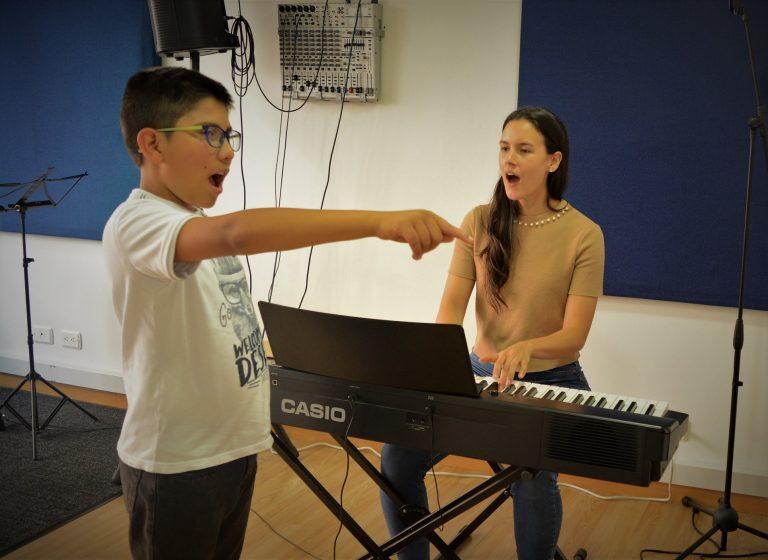 Niño en clase de canto con profesora sentada al piano