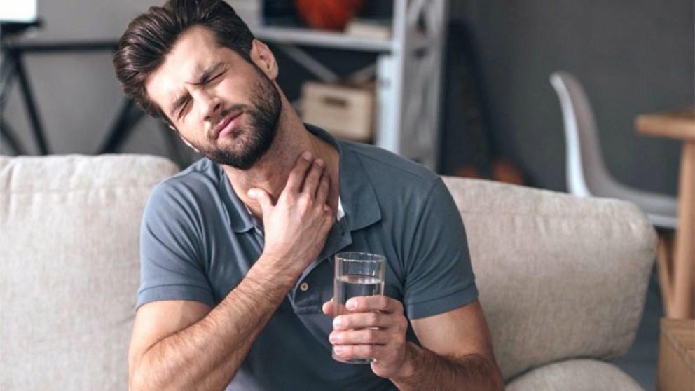 hombre sentado con dolor de garganta, tocándose el cuello