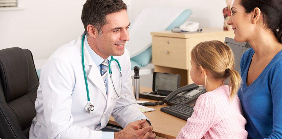 Foniatra escuchando a una niña sentada en las piernas de su madre, en medio de una consulta