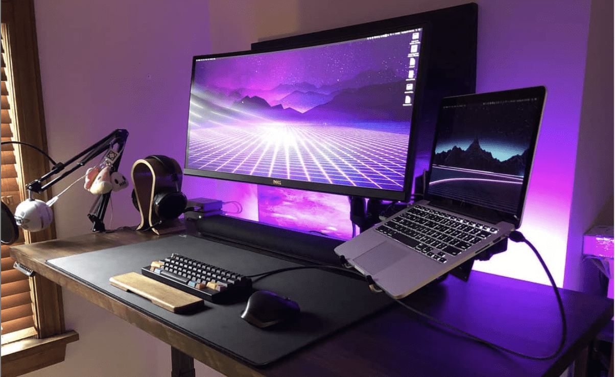 Monitor grande sobre un escritorio, junto a un portatil. Habitación de color magenta.